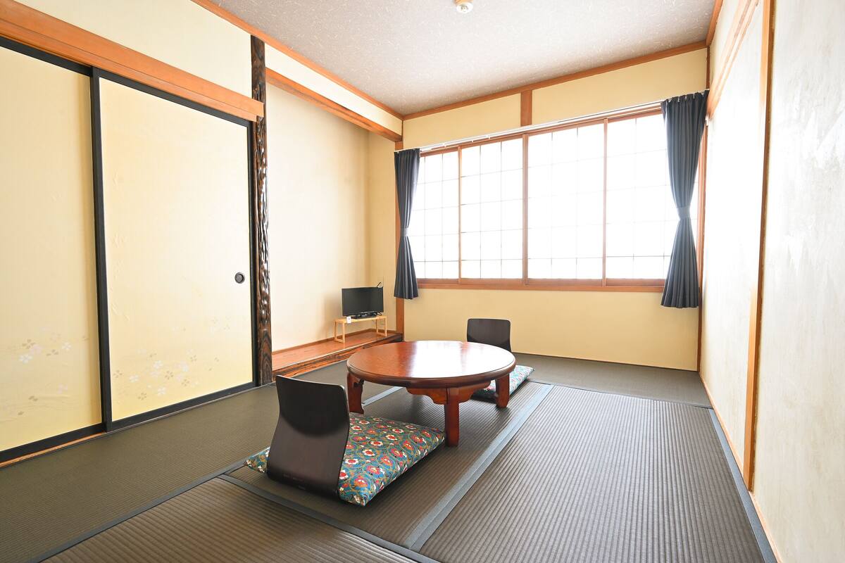 A traditional Japanese room with tatami flooring, a low table, and a TV on a shelf.