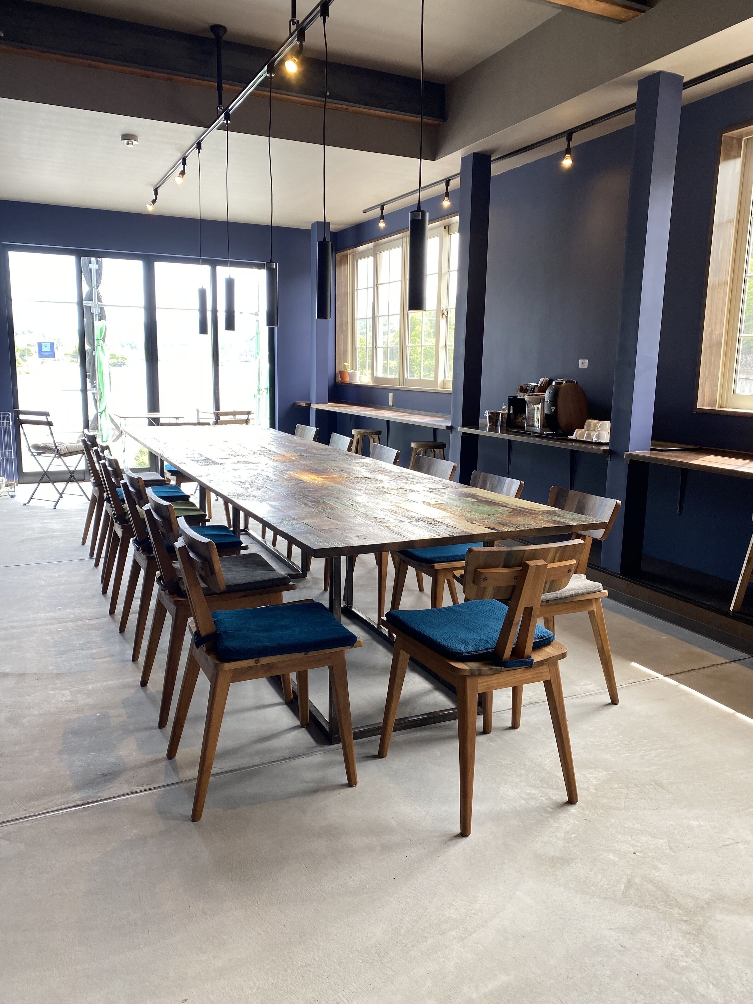 A spacious dining area with a long wooden table and chairs, large windows, and hanging pendant lights.