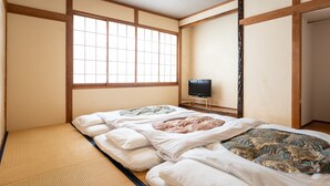 A traditional Japanese room with tatami flooring, a futon bed, a television, and a sliding door. - Mountain Lodge at 1,400m Hütte Jil Shirakabako (Chino)