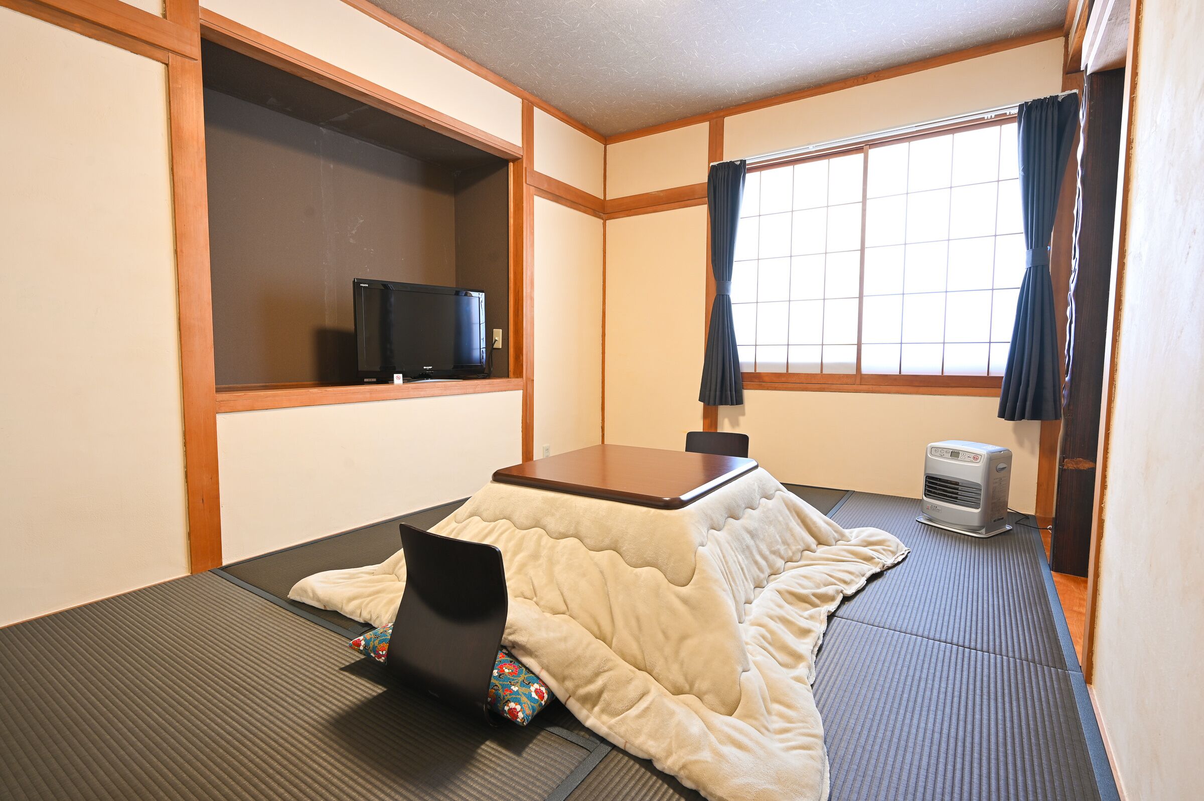 A room with tatami flooring, a futon bed, a television on a shelf, and a heater.