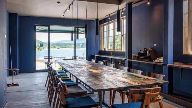 A long wooden table with chairs, large windows, and a view of a lake. - Mountain Lodge at 1,400m Hütte Jil Shirakabako (Chino)