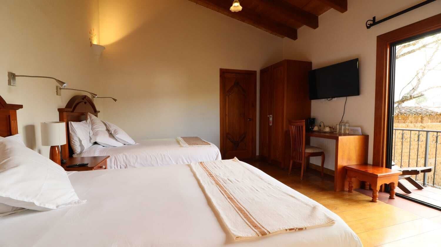 A hotel room with two beds, a desk, a chair, and a TV mounted on the wall.
