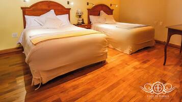 Una camera da letto con due letti, pavimento in legno e un comodino con una lampada.
