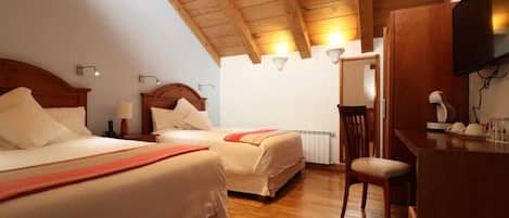 Une chambre d’hôtel avec deux lits, des poutres apparentes en bois au plafond, un bureau avec une chaise et un téléviseur.