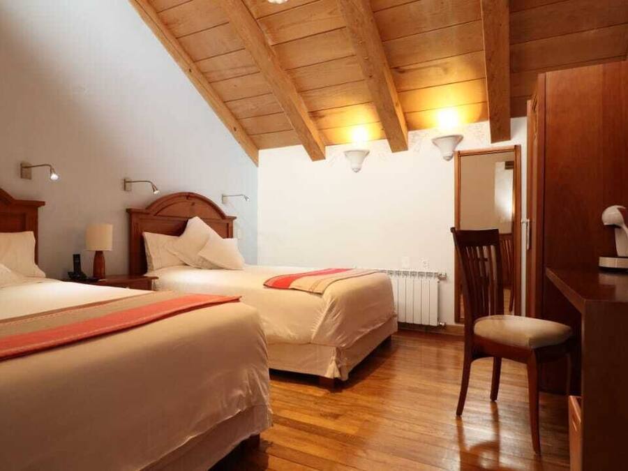 Habitació d'hotel amb dos llits, bigues de sostre de fusta, escriptori amb cadira i televisió.