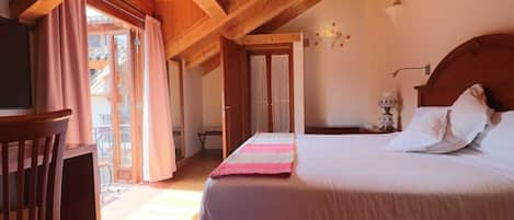 Un dormitorio con techo de madera, una cama con ropa blanca, una manta a rayas rosa y gris, una silla de madera y una ventana con cortinas.