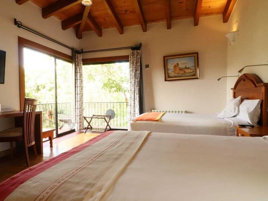 A hotel room with two beds, a TV, a balcony with a chair, and a painting on the wall.