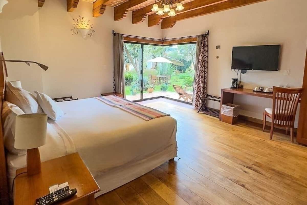 Quarto com cama grande, escrivaninha, televisão e porta de vidro deslizante para um pátio.