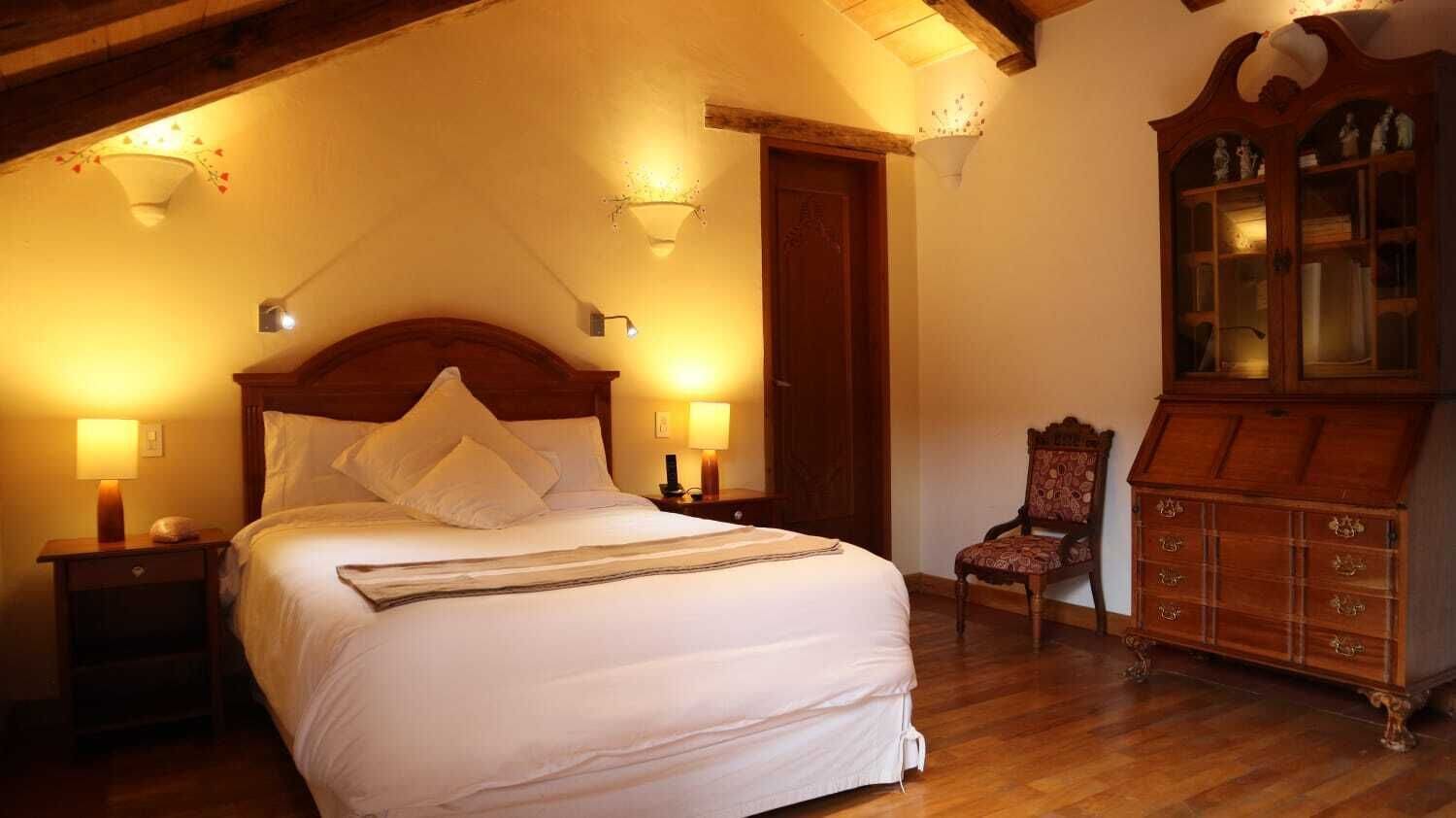 A bedroom with a large bed, two bedside lamps, a wooden dresser, and a chair.
