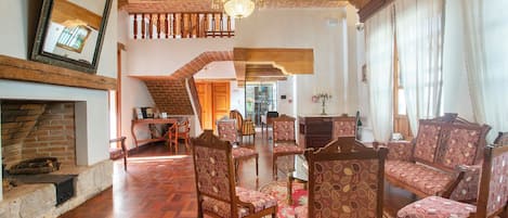 Amplia sala de estar con piso de madera, sillas estampadas, chimenea y candelabro.