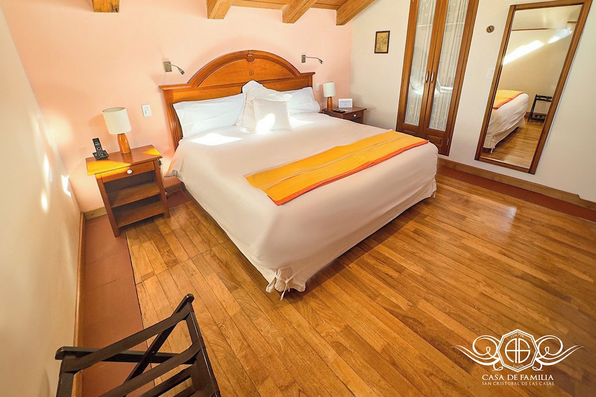 Quarto com cama de madeira, mesas de cabeceira, espelho e cadeira de madeira.