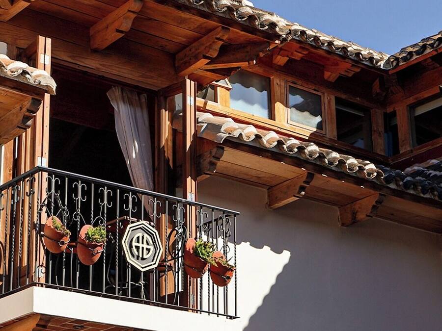 A wooden balcony with terracotta tiles, potted plants, and a metal railing.