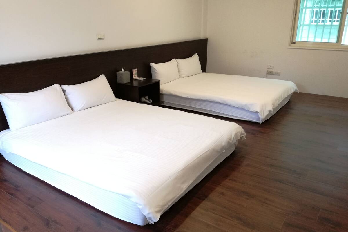 A hotel room with two single beds, a nightstand, and a window with bars.