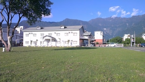 A building with a flat roof and a central entrance, surrounded by a grassy area and trees. - Oak Garden Hotel (Hualien City)