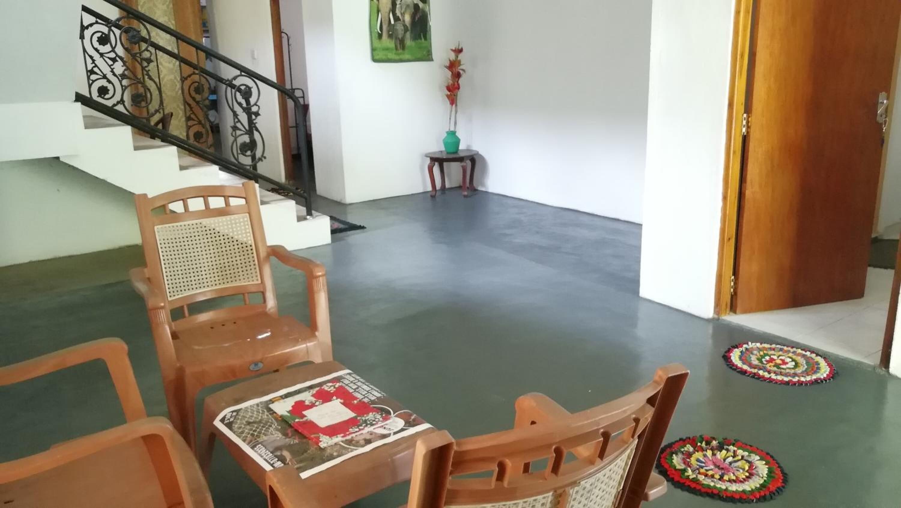 A room with a wooden chair and a small table, a staircase with a metal railing, and a door.