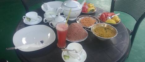 Une table ronde sur laquelle on trouve différents plats, notamment un saladier de fruits, un bol de lentilles et un verre de jus.