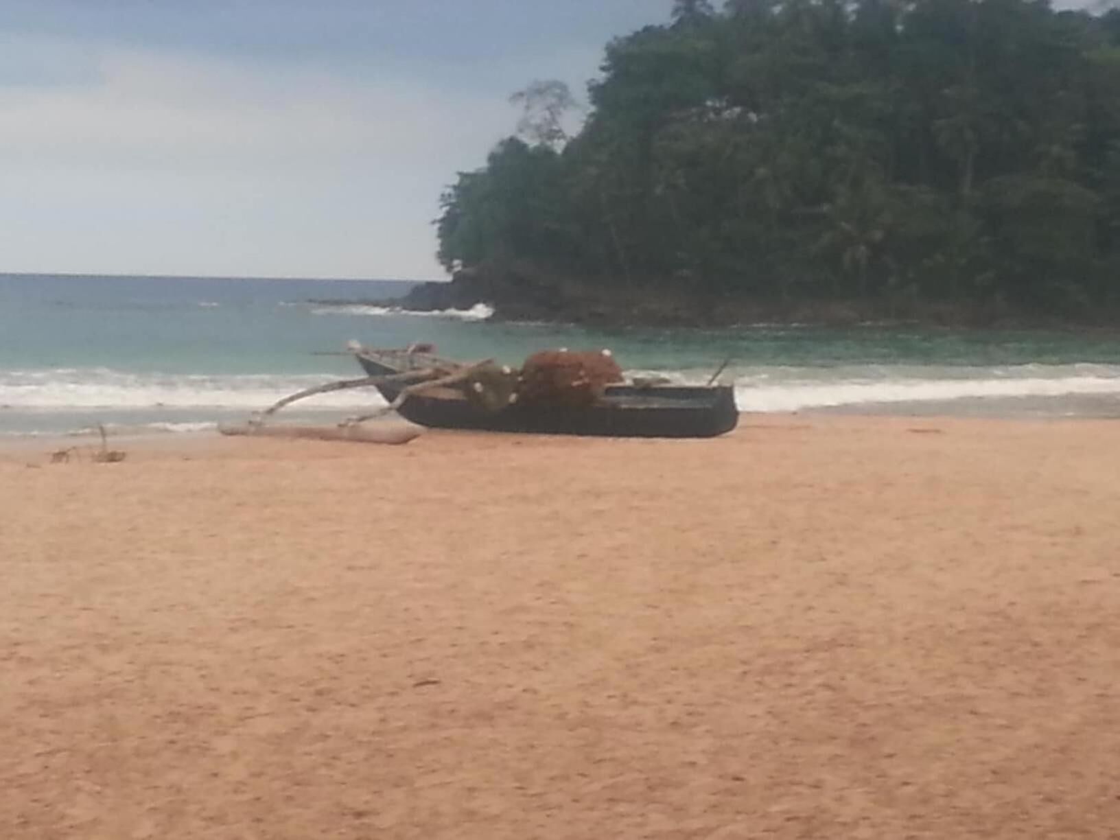 A beach with a boat on the sand and a forested area in the background.