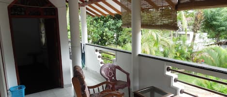 A covered balcony with a wooden chair, a small table, and a view of greenery.