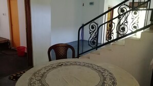 Una habitación con una mesa redonda con un borde decorativo, una silla de madera, una cesta de plástico roja y una escalera con barandillas de metal ornamentadas.