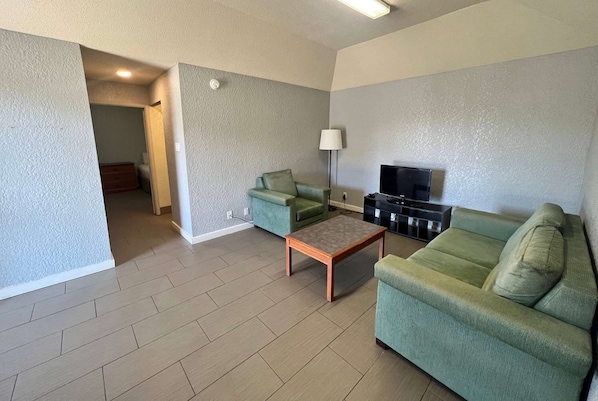 Una sala de estar con sofá, mesa de centro, mueble para televisión y lámpara.