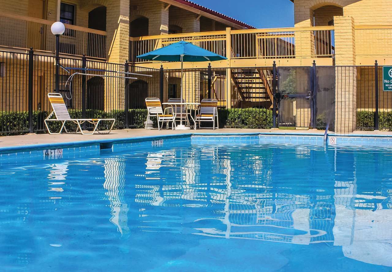 A swimming pool with lounge chairs and umbrellas, surrounded by a building with a balcony and a staircase.