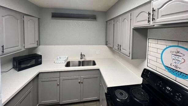 A kitchen with white cabinets, a black microwave, a sink, and a stove.