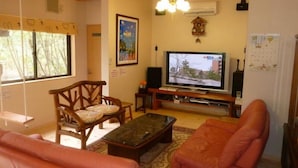 A cozy living room with wooden furniture, a television, and a ceiling fan. - Heart Land Hills Fairy tale house (Shika)