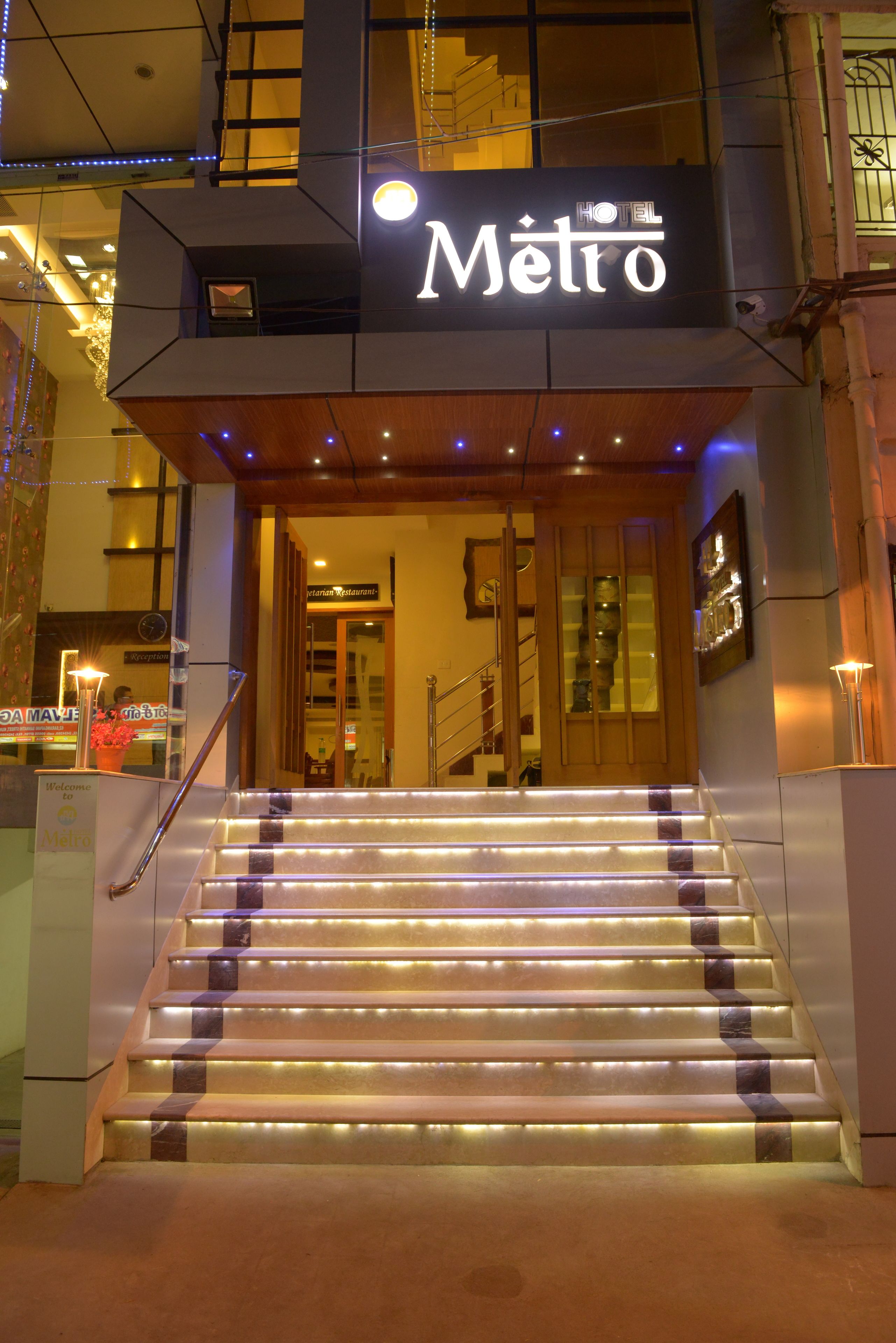 A hotel entrance with a sign reading "Hotel Metro," a staircase with illuminated steps, and a reception desk.
