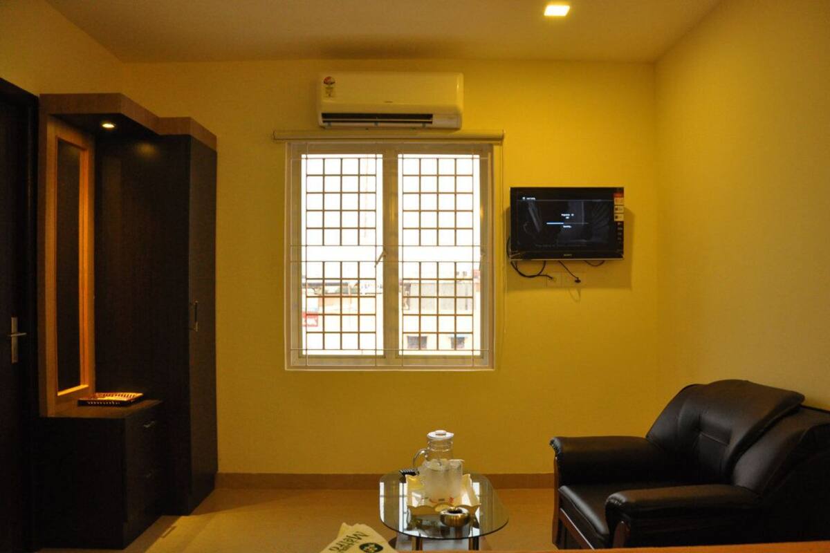 A living room with a TV mounted on the wall, a window with bars, a black leather sofa, and a small table with a decorative item.