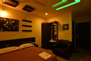 A hotel room with a bed, a chair, a painting on the wall, and a minibar. - Hotel Metro (Kumbakonam)
