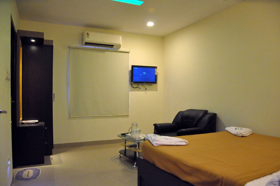 A hotel room with a bed, a desk, a chair, a television, and an air conditioning unit.