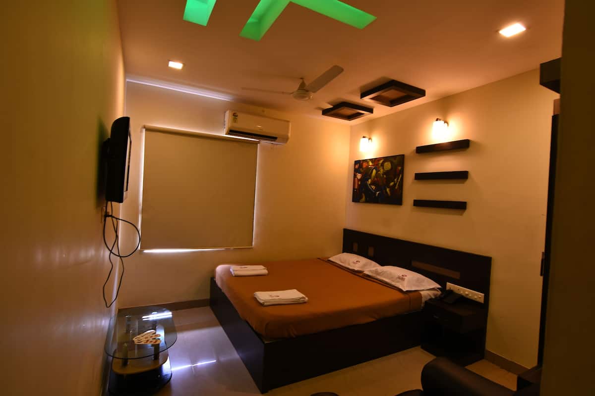A modern hotel room with a bed, bedside table, wall-mounted air conditioning unit, ceiling fan, and artwork on the wall.