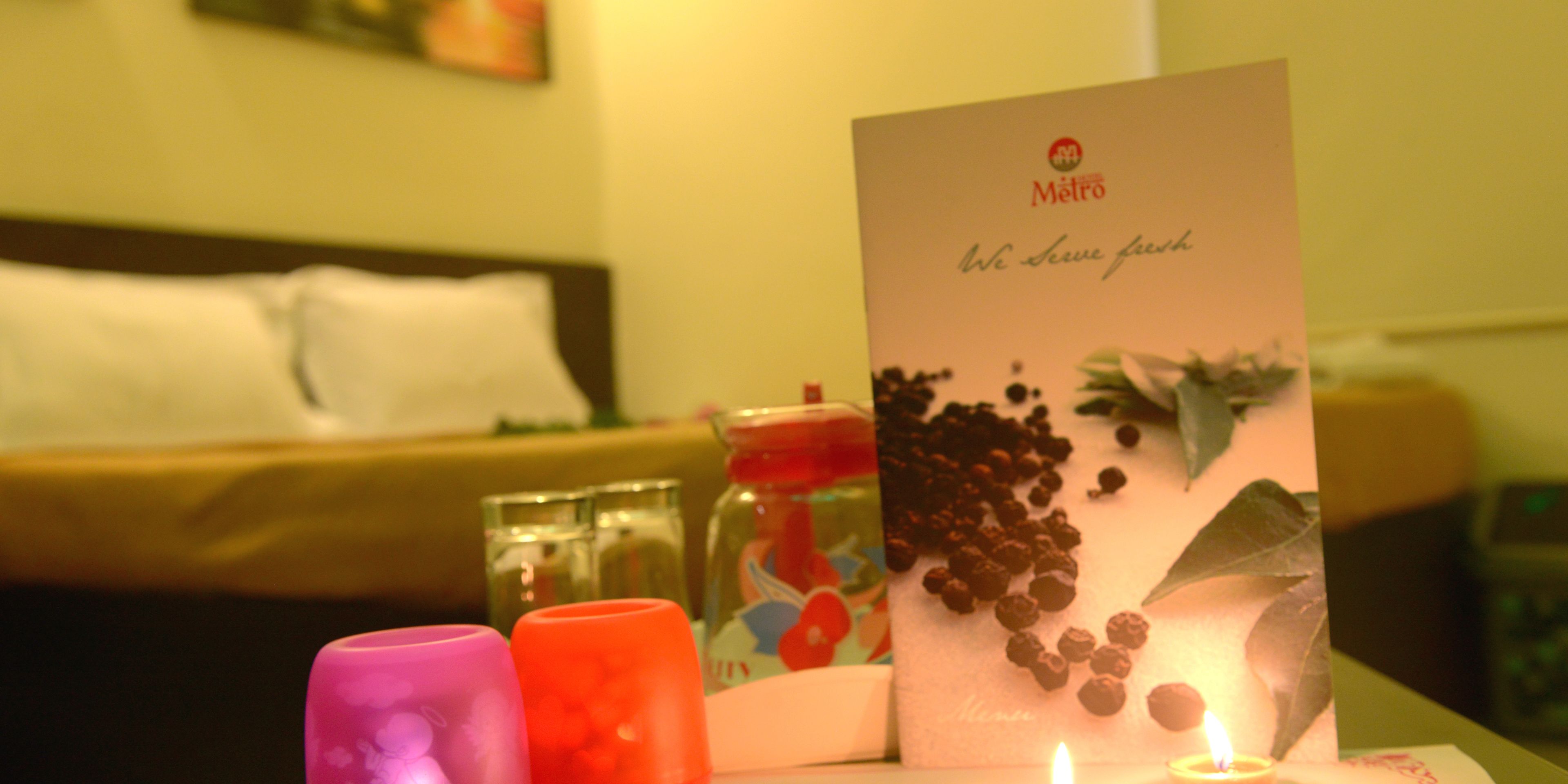 A hotel room with a bed, a card on the table, and two candles.