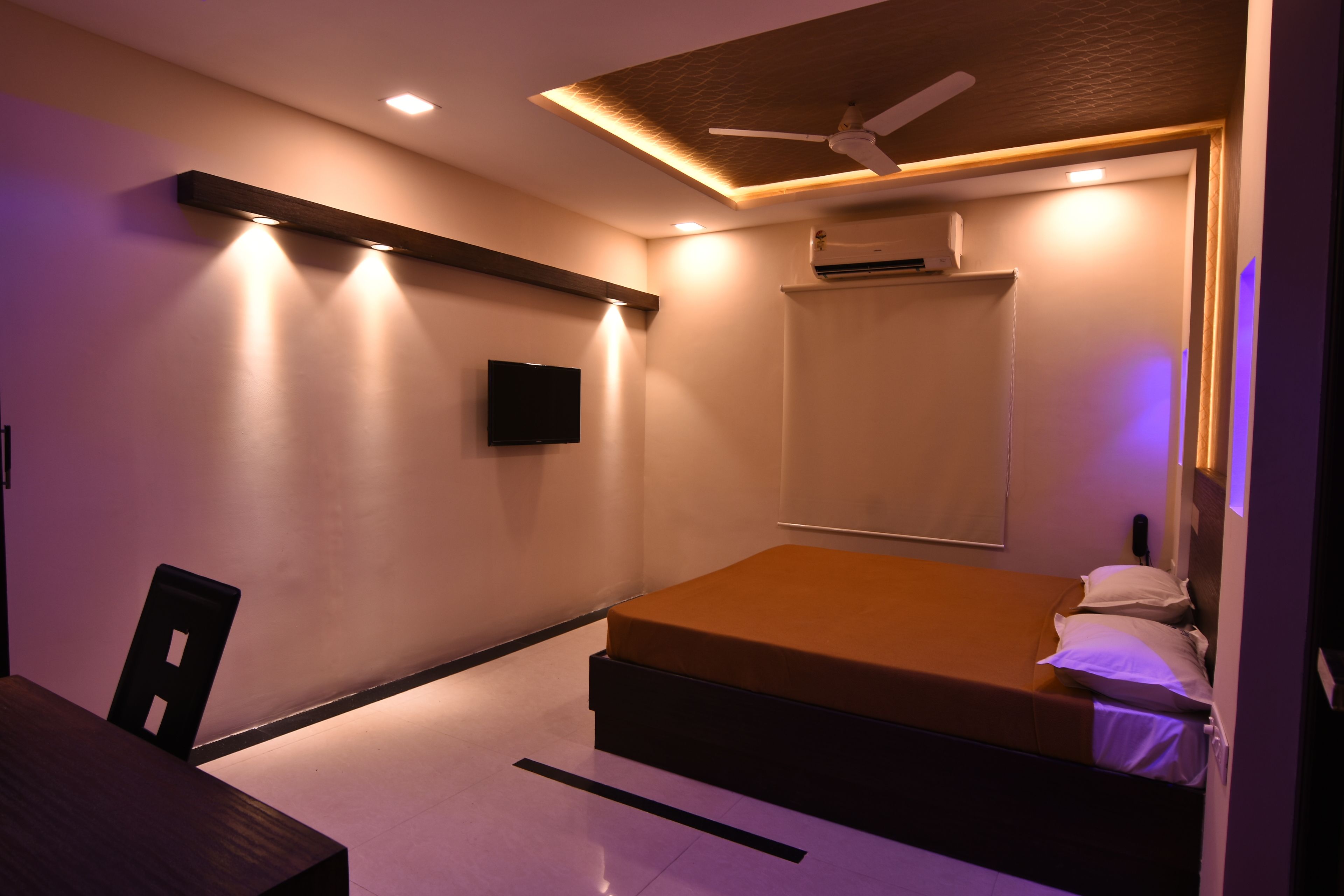 A modern bedroom with a bed, a desk, and a chair. There is a ceiling fan and recessed lighting.