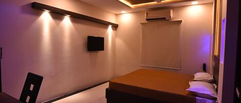 A modern bedroom with a bed, a desk, and a chair. There is a ceiling fan and recessed lighting.