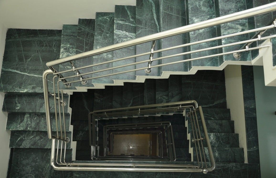 A set of dark marble stairs with a metal handrail and a central spiral staircase.