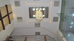 Un interior moderno con una araña central, barandilla de vidrio y un panel de pared de madera.