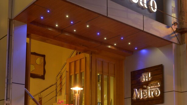 Entrada de hotel con un letrero que dice "Metio", una escalera con escalones iluminados y un cartel de bienvenida.