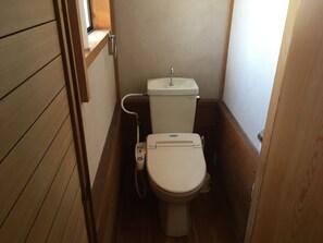 A compact bathroom with a toilet, a hand sanitizer dispenser, and a window above the toilet. - Heart Land Hills View of yacht harbor house (Nanao)