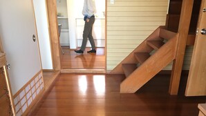 A wooden staircase leading to an upper floor, a wooden floor, and a kitchen area in the background. - Heart Land Hills View of yacht harbor house (Nanao)