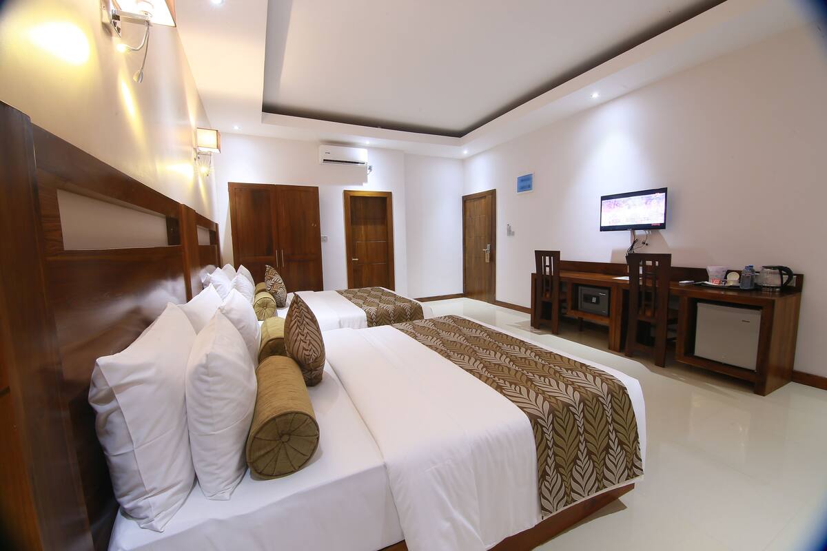 Habitación de hotel con dos camas, un escritorio, un televisor y una kitchenette pequeña.