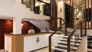 Un espace d’accueil d’hôtel comprenant un comptoir de réception en bois, un escalier avec une rampe en verre et un panneau décoratif mural.