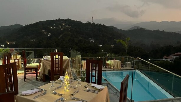 Une table à manger dressée pour deux personnes, avec vue sur une montagne et une piscine en arrière-plan.