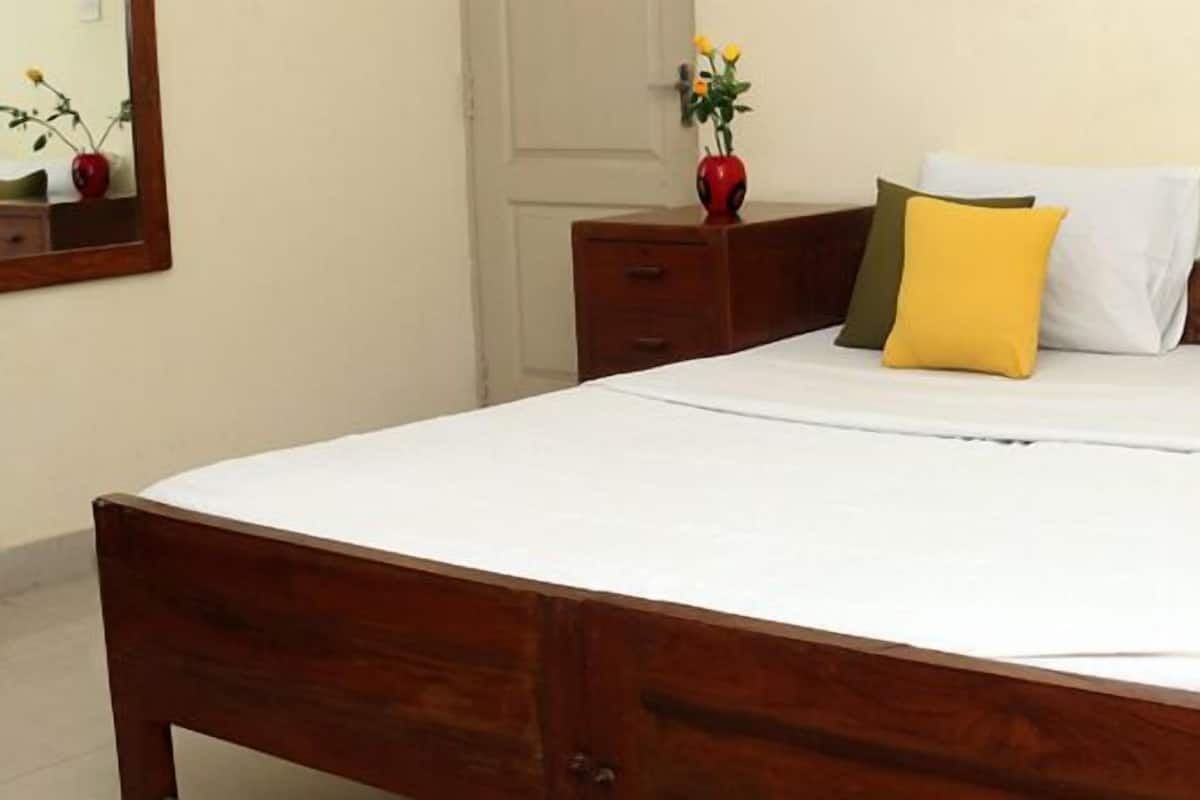 A neatly made bed with white bedding and two pillows, a wooden nightstand with a vase of flowers, and a mirror on the wall.
