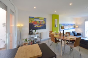 A modern dining area with a wooden table, chairs, and a glass partition. There are potted plants and a painting on the wall.