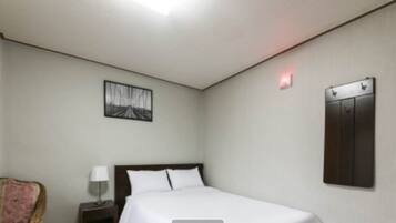 A hotel room with a bed, a nightstand with a lamp, a chair, a wall-mounted cabinet, and a framed picture on the wall.