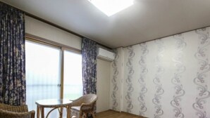 A room with a large window, a small round table, two wicker chairs, and patterned wallpaper. - Namwon Hotel (Namwon)