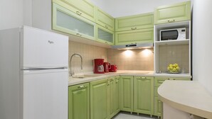 A kitchen with green cabinets, a white refrigerator, a microwave, and a sink. - Apartments Center (Belgrade)