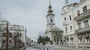 A street view with a prominent church tower, a white building with a clock, and a building with a balcony. - Apartments Center (Belgrade)