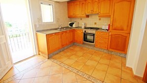 A kitchen with wooden cabinets, a microwave, a stove, and a tiled floor. - Casa del Campo - sea view villa with private pool in Moraira (Moraira)